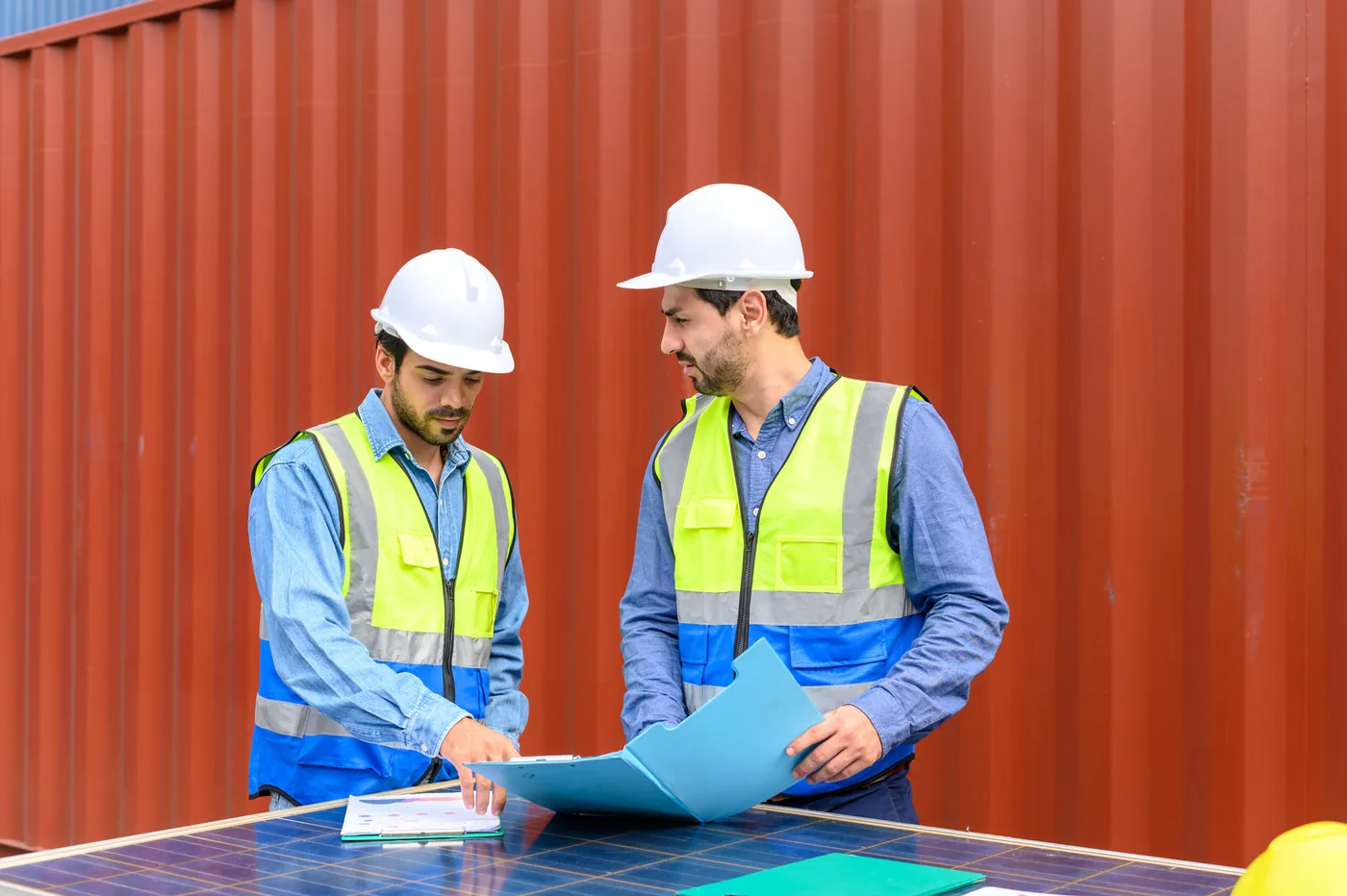 Two Logitera supervisors in high-visibility vests reviewing paperwork beside a shipping container