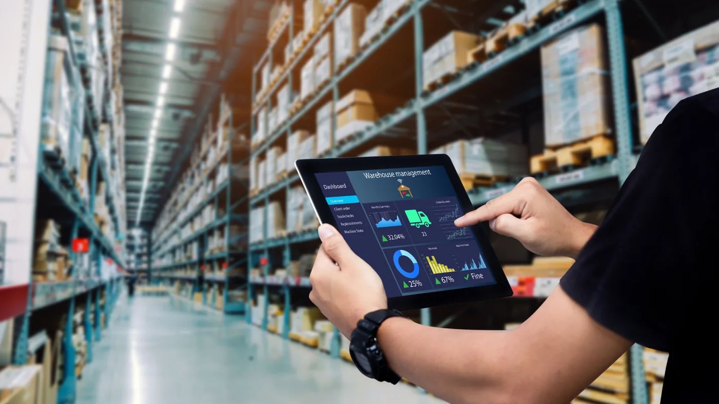 Operator reviewing a live inventory dashboard on a tablet inside a high-bay warehouse aisle